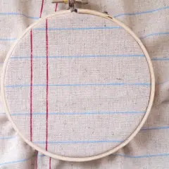 Bastidor de bordar sobre tela de lino con líneas rojas y azules, ideal para tus proyectos de hogar manualidades para casa.