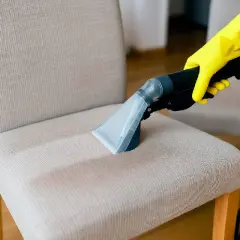 Mano con guante amarillo usa aspiradora para limpiar silla de tela, mostrando cómo quitar manchas de sillas de tela.