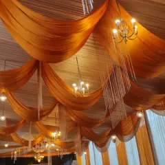 Techo con telas naranjas y blancas, adornado con candelabros y colgantes de cristal.