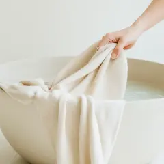 Mano sumerge tela clara en agua para lavar ropa blanca.