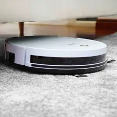 Robot aspirador blanco y negro limpiando alfombra gris, ideal para saber como eliminar los acaros del hogar.