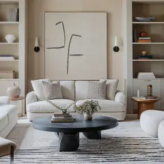 Salones blancos con sofás cómodos, mesa de centro oscura y arte abstracto. Estanterías llenas de libros y objetos decorativos.