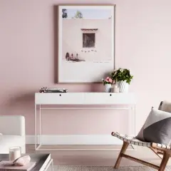 Un salón con paredes rosas, un sofá blanco, una consola con flores y un cuadro. El rosa se combina con blanco, gris y madera para un ambiente sereno.