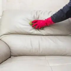 Mano con guante rosa limpiando un sofá de cuero beige con una esponja. Aprende cómo limpiar sofá de cuero para mantenerlo como nuevo.