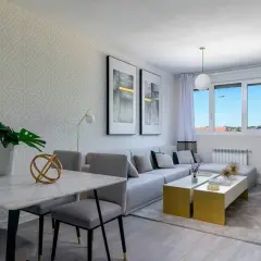 Salón rectangular dos ambientes con mesa de mármol, sofá modular gris y mesas doradas.