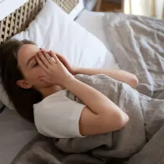 Mujer en la cama, con las manos cubriendo su rostro, luchando contra el miedo a quedarse dormido.