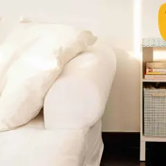 Sofá blanco con cojines y estantería con libros y cestas. Ideas para como hacer funda sofa.