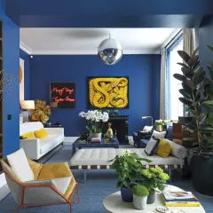 El azul vibrante de las paredes crea un telón de fondo audaz. El amarillo mostaza y el blanco puro son colores que combinan con el azul, aportando calidez y luminosidad a este salón moderno.