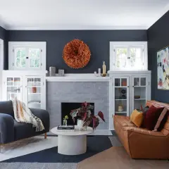 Ideas para decorar rincones pequeños: un sofá de cuero, sillón gris, chimenea y arte abstracto en un salón moderno.