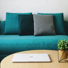 Un sofá moderno color turquesa, con cojines en tonos oscuros y un patrón de pata de gallo. Un portátil y una planta decoran la mesa de centro. ¡Perfecto para teñir el sofá de un nuevo color!