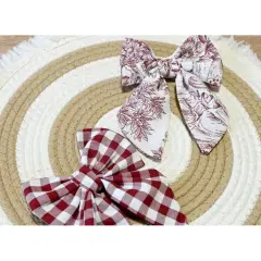 Dos lazos de tela, uno a cuadros rojos y blancos, otro con estampado floral en tonos burdeos, descansan sobre un tapete circular de cuerda.
