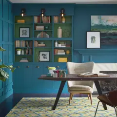 Estudio con paredes y estanterías en azul petróleo, combinación perfecta con detalles verdes. Alfombra geométrica y mobiliario moderno.