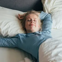 Mujer rubia sonríe plácidamente en su cama, disfrutando de un sueño reparador bajo la suave roba de llit.