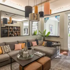 Amplios salones con sofás modulares grises, cojines coloridos y una mesa de centro. Reflejos en espejos y lámparas colgantes añaden estilo.