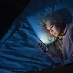 Mujer rubia en la cama, mirando su móvil con luz azul. Quizás por eso me despierto a las 4 de la mañana.