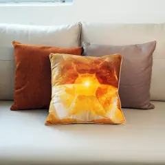 Tres cojines sobre un sofá de cuero: uno naranja texturizado, uno con un diseño de cristal amarillo brillante y otro marrón. El cojín central, con su estampado de velour que es, irradia calidez.