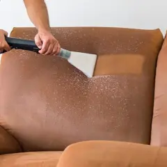 Hombre usando una aspiradora con una mezcla para limpiar sofá. El sofá de gamuza marrón se ve limpio y fresco.