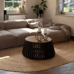 Alfombra redonda de yute planta bajo un sofá modular beige. La luz del sol ilumina la sala.