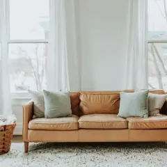 Sofá de cuero marrón con cuatro cojines, dos claros y dos más oscuros, ideal para saber cuántos cojines poner en un sofá y crear un ambiente acogedor.