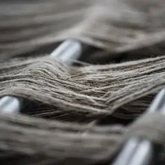 Fibras sintéticas ejemplos: hilos grises entrelazados sobre barras metálicas, creando una textura visual rica y detallada.