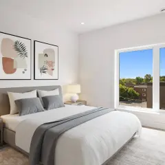 Dormitorio moderno con cama canapé vestida con ropa de cama blanca y gris, mesitas de noche y cuadros abstractos.
