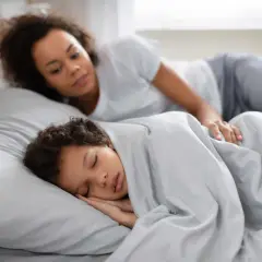 Madre observa a su hijo dormir plácidamente. Quizás se pregunta por qué se habla en sueños, o simplemente disfruta de la paz del momento.