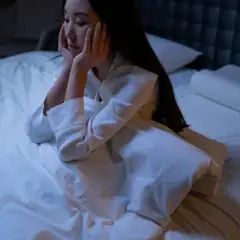 Me despierto de madrugada y no puedo volver a dormir. Una mujer sentada en la cama, con las manos en la cara, mirando al vacío.