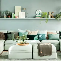 Sofá modular con cojines en tonos verdes y marrones, creando una paleta de colores que combinan con turquesa. Plantas y objetos decorativos en una estantería superior.