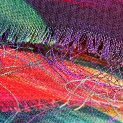 Detalle de tela con hilos sueltos de colores vibrantes. Se aprecia el tejido y cómo se puede coser a mano para que no se deshilache.