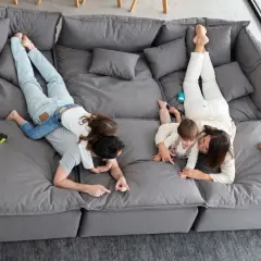 Familia jugando en un cómodo sofá gris. Los niños se divierten sobre sus padres mientras descansan en este amplio sofá.