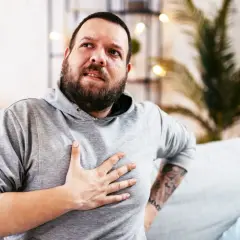 Hombre con barba, con la mano en el pecho, con expresión de dolor. Estaba durmiendo y de repente me desperté sin poder respirar.