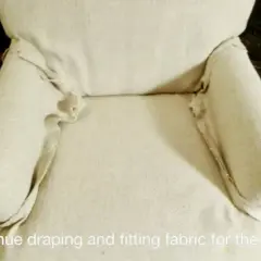 Tela beige drapeada y ajustada con alfileres en los brazos de una silla, parte de un tutorial sobre como hacer fundas para sillas.