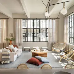 Un salón estilo industrial nórdico con sofá blanco, mesas de centro de madera, sillas de ratán y grandes ventanales.
