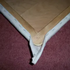 Detalle de cómo tapizar esquinas de un bastidor de madera con tela blanca, asegurada con grapas.