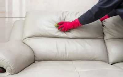 Mano con guante rosa limpiando un sofá de cuero beige con una esponja. Aprende cómo limpiar sofá de cuero para mantenerlo como nuevo.