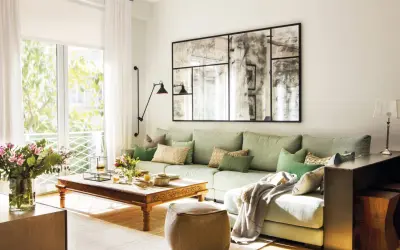 Un puf de terciopelo marrón es una opción acogedora que poner al lado del sofá, junto a una mesa de centro de madera y un sofá verde claro.