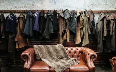 Abrigos de cuero colgados sobre un sofá Chesterfield. Si el cuero huele, aquí te explicamos como quitar el olor a cuero.