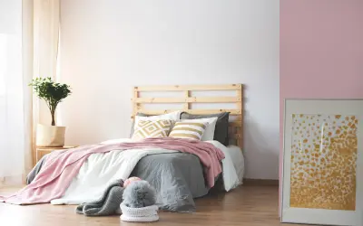 Dormitorio acogedor donde el beige y rosa combinan a la perfección en mantas y cojines. Una planta aporta frescura.