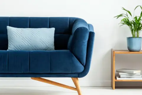 Sofá azul profundo con cojín claro. Un toque de color turquesa en la decoración con una planta y libros en una mesita de madera.