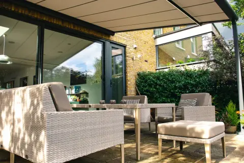 Mobiliario de exterior y plantas crean un espacio acogedor. Ideas para separar terrazas con estilo y privacidad.