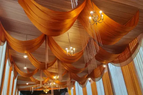 Techo con telas naranjas y blancas, adornado con candelabros y colgantes de cristal.