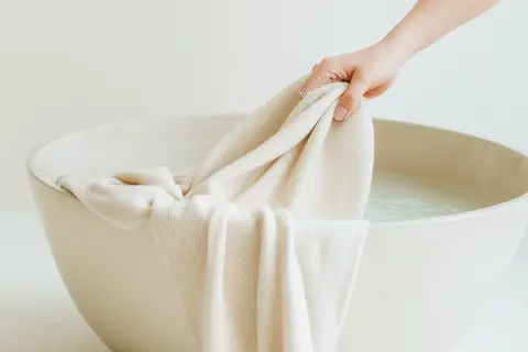 Mano sumerge tela clara en agua para lavar ropa blanca.