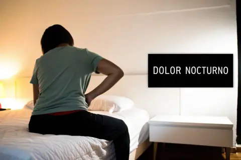 Persona con dolor de espalda sentada en la cama, buscando cómo dormir con hernia discal. El letrero dice "DOLOR NOCTURNO".