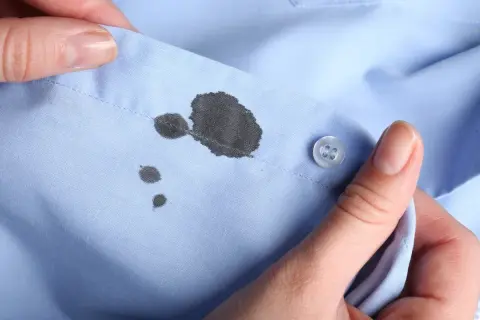 Manos sujetan camisa azul con manchas de boli. Aprende como quitar manchas de boli fácilmente.