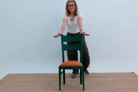 Mujer sonriente muestra cómo forrar sillas con estilo, usando una silla verde con cojín naranja.