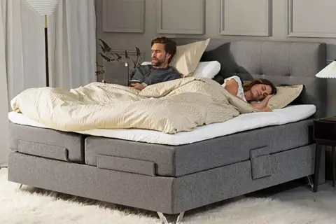 Hombre despierto en cama con portátil, mujer durmiendo a su lado. Un momento de paz para dormir juntos.