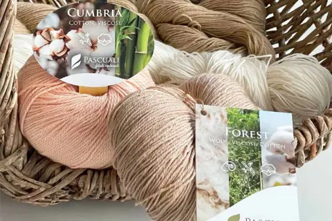 Ovillos de lana y fibras artificiales, como viscosa, en tonos naturales dentro de una cesta de mimbre.