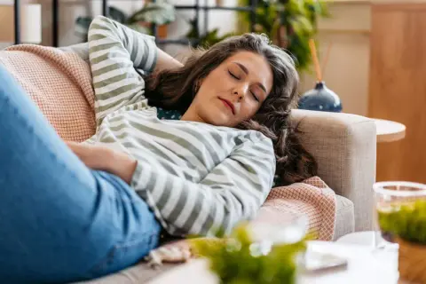 Mujer descansando en el sofá, con los ojos cerrados, lista para dormir antes de comer.