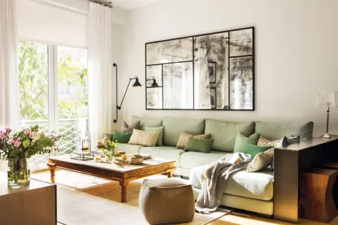 Un puf de terciopelo marrón es una opción acogedora que poner al lado del sofá, junto a una mesa de centro de madera y un sofá verde claro.