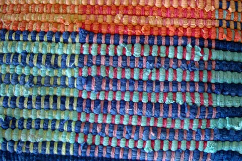 Textura de alfombra tejida a mano con hilos de colores: naranja, azul y verde. Ideal para aprender como hacer una alfombra.